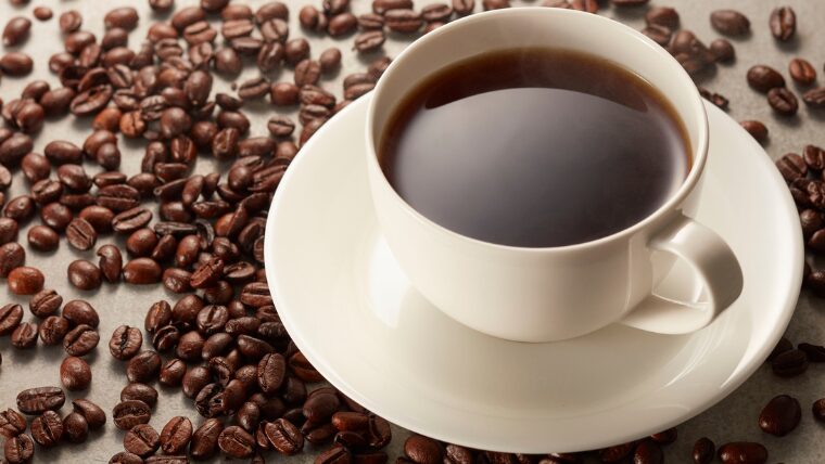 カップに入った一杯のコーヒーと、周りに散らばったコーヒー豆