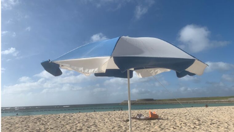 トロピカルビーチの砂浜にパラソルが立っている。エメラルドグリーンの海と青い空。