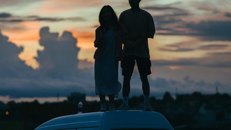 車の屋根に乗って景色を眺める男女